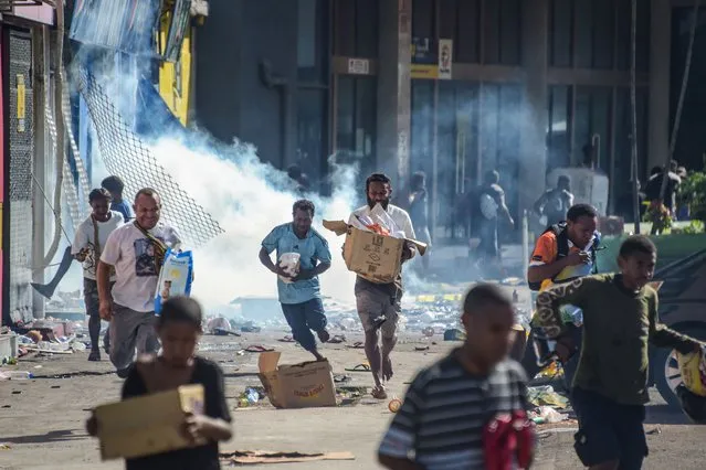 People run with merchandise as crowds leave shops with looted goods amid a state of unrest in Port Moresby on January 10, 2024. A festering pay dispute involving Papua New Guinea's security forces on January 10 sparked angry protests in the capital, where a crowd torched a police car outside the prime minister's office. By Wednesday afternoon pockets of unrest had spread through the capital Port Moresby, with video clips on social media showing crowds looting shops and stretched police scrambling to restore order. (Photo by Andrew Kutan/AFP Photo)