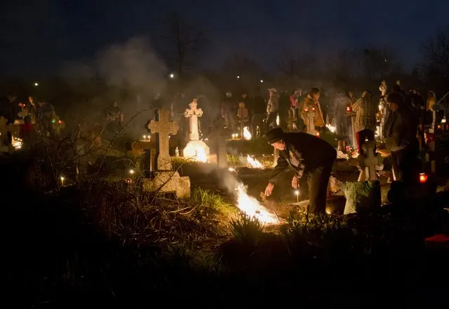 People stand by fires they lit by a relative's grave in a cemetery during an Orthodox Palm Sunday memorial for the departed in Herasti, southern Romania, early Sunday, April 5, 2015. Orthodox believers gather at midnight, light fires at the graves and share food in memory of their dead relatives. (Photo by Vadim Ghirda/AP Photo)