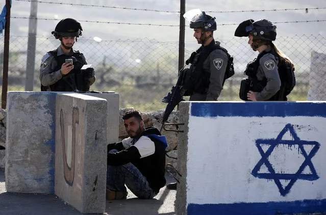 Israeli border police have an arrested Palestinian ordered to sit down on the ground while checking his identity at a checkpoint in Beit Enoon, near the West Bank city of Hebron, 04 April 2016. The man reportedly was arrested within the usual security measures taken in the region by the Israeli forces. (Photo by Abed Al Hashlamoun/EPA)