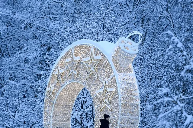 A woman walks past a light arch set up for the upcoming New Year and Christmas holidays in front of snow covered trees after heavy snowfall in Moscow outskirts on December 14, 2021. (Photo by Kirill Kudryavtsev/AFP Photo)