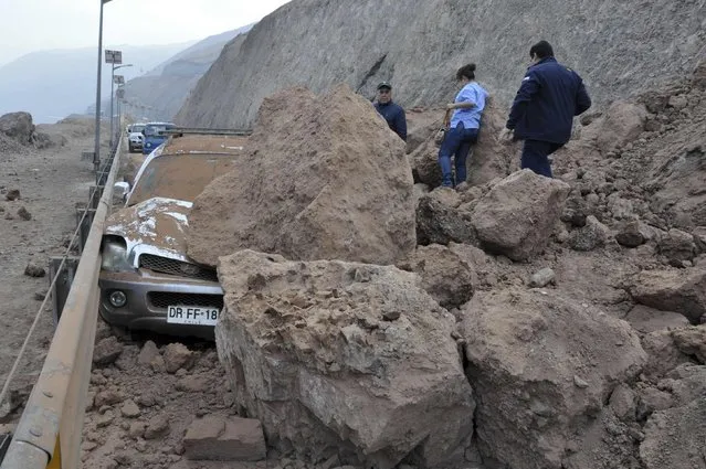 Rescue workers inspect a car caught under a landslide after an earthquake and tsunami hit the northern port of Iquique, April 2, 2014. The earthquake, with a magnitude of 8.2, struck off the coast of northern Chile near the copper exporting port of Iquique on Tuesday evening, killing six and triggering the tsunami that pounded the shore with 2-meter (7-foot) waves. (Photo by Cristian Vivero/Reuters)