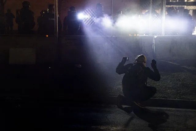 Police shine lights on demonstrator with raised hands during a protest over Sunday's fatal shooting of Daunte Wright during a traffic stop, outside the Brooklyn Center Police Department on Wednesday, April 14, 2021, in Brooklyn Center, Minn. (Photo by John Minchillo/AP Photo)