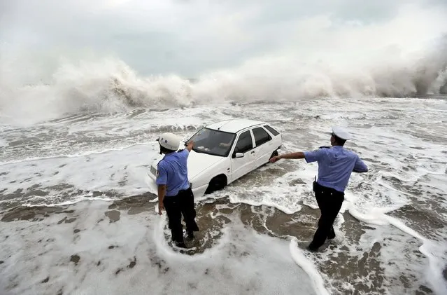 Policemen gesture to a driver stranded in a car on a flooded road as waves are whipped up by typhoon Bolaven in Qingdao, Shandong province, August 28, 2012. Gales and downpours brought by typhoon Bolaven swept through parts of northeast China from Tuesday evening to Wednesday, flooding cities and delaying flights, Xinhua News Agency reported. (Photo by Reuters/China Daily)