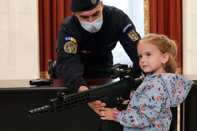 A girl poses with a weapon at a stand set up by Romania's gendarmerie at the Palace of the Parliament, the second largest administrative building in the world after the Pentagon, as people took advantage of the opportunity to visit it for free on International Children's Day in Bucharest, Romania, Tuesday, June 1, 2021. More than ten thousand children and adults visited the communist era building, also known as the House of the People, according to the organizers of the event. (Photo by Vadim Ghirda/AP Photo)