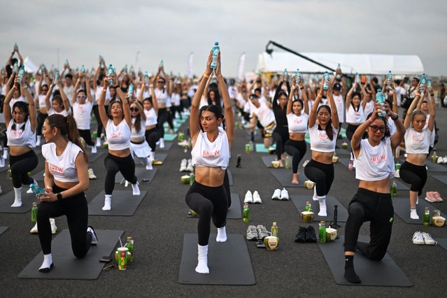 Yoga enthusiasts perform yoga during a sunrise “Brew Yoga” event on a runway at Suvarnabhumi Airport in Bangkok on April 27, 2024. Stretching their fingertips to the reddening sky, hundreds of yoga devotees rolled out their mats on the runway of Bangkok's main airport, practising their downward dog as early morning flights rumbled overhead. (Photo by Manan Vatsyayana/AFP Photo)