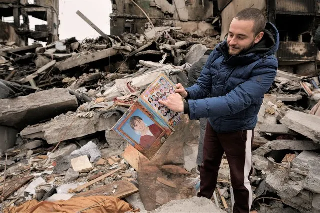 Dmitriy Evtushkov, 25, points to his picture in a primary school album retrieved from the rubble of an apartment building destroyed during fighting between Ukrainian and Russian forces in Borodyanka, Ukraine, Tuesday, April 5, 2022. Ukrainian President Volodymyr Zelenskyy accused Russian troops of gruesome atrocities in Ukraine and told the U.N. Security Council on Tuesday that those responsible should immediately be brought up on war crimes charges in front of a tribunal like the one set up at Nuremberg after World War II. (Photo by Vadim Ghirda/AP Photo)