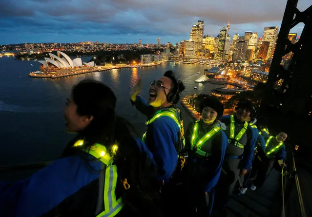 Participants wear glowing vests as they look out to the Sydney Opera House from the Sydney Harbour Bridge in Australia during a press preview of the Vivid Climb Mandarin for Chinese-language tours of the Sydney icon on May 18, 2017. (Photo by Jason Reed/Reuters)