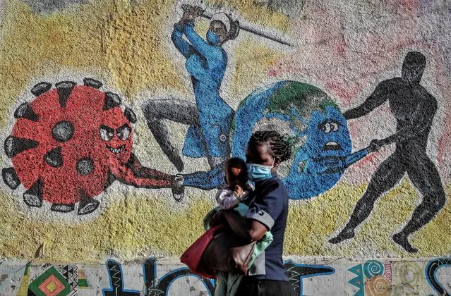 A woman and child walk past an informational mural portraying the global battle against the coronavirus, on a street in Kericho, Kenya on January 26, 2022. The World Health Organization said Thursday, April 14, 2022 that the number of coronavirus cases and deaths in Africa have dropped to their lowest levels since the pandemic began, marking the longest decline yet seen in the disease. (Photo by Brian Inganga/AP Photo/File)