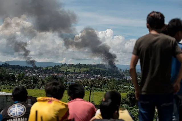 People watch as smoke billows from houses after aerial bombings by Philippine Airforce planes on Islamist militant positions in Marawi on the southern island of Mindanao on June 17, 2017. Philippine troops pounded Islamist militants holding parts of southern Marawi city with air strikes and artillery on June 17 as more soldiers were deployed and the death toll rose to more than 300 after nearly a month of fighting. (Photo by Noel Celis/AFP Photo)