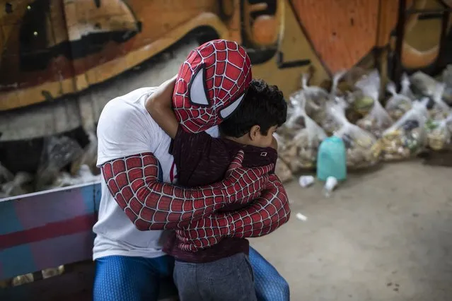A volunteer dressed as Spiderman embraces a child in the Jardim Gramacho favela of Rio de Janeiro, Brazil, Saturday, October 30, 2021, during a food kit delivery donated by the non-governmental organization “Covid Sem Fome” that works to fight hunger. (Photo by Bruna Prado/AP Photo)