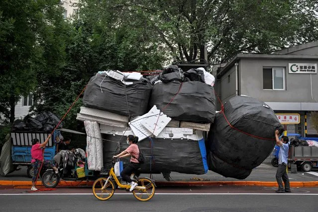 Two workers load a large sack of foam on a tricycle in front of a waste sorting site in Beijing on June 21, 2022. (Photo by Jade Gao/AFP Photo)