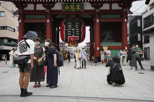 A rickshaw puller helps visitors take their photos as he promotes his business in front of the famed Kaminarimon gate of Sensoji Buddhist temple in Tokyo's Asakusa area famous for sightseeing, Wednesday, June 22, 2022. (Photo by Hiro Komae/AP Photo)
