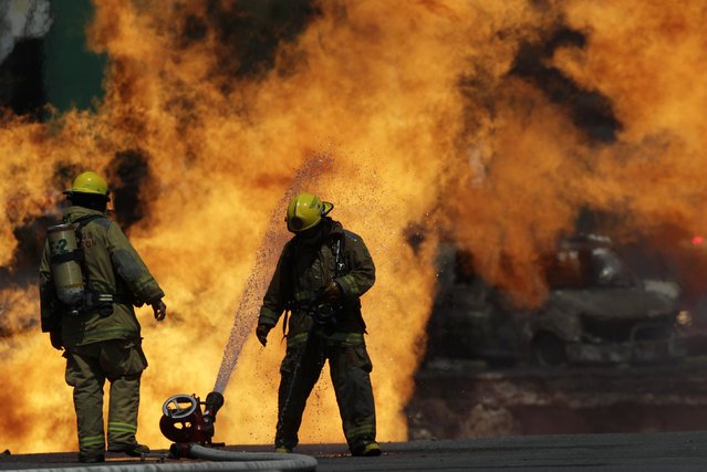 An uncontrolled fire burns behind firefighters, one of them cooling himself with a water hose, in San Pedro Garza Garcia, on the outskirts of Monterrey August 7, 2014. A gas pipeline exploded causing the rupture of a street in a commercial area of San Pedro Garza Garcia and destroying three cars but nobody was killed or injured, according to local media. (Photo by Daniel Becerril/Reuters)
