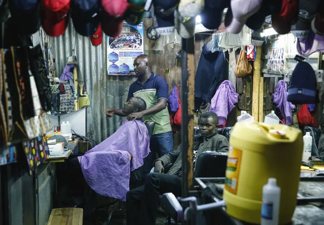 In this photo taken Tuesday, March 24, 2020, a barber continues his trade despite the fear of the new coronavirus, saying “It's better to die sick than die hungry”, in the Mathare slum, or informal settlement, of Nairobi, Kenya. Many slum residents say staying at home or social-distancing is impossible for those who live hand to mouth, receiving daily wages for informal work with no food or economic assistance from the government, as is maintaining sanitation where a pit latrine can be shared by over 50 people. The new coronavirus causes mild or moderate symptoms for most people, but for some, especially older adults and people with existing health problems, it can cause more severe illness or death. (Photo by Brian Inganga/AP Photo)