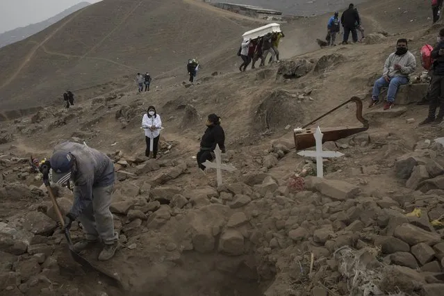 A cemetery worker shovels dirt into a grave that contains the remains of Apolonia Uanampa who died from the new coronavirus, as the coffin that contains the remains of Demetria Huamani, also a victim of the virus, is carried to her burial site at the Nueva Esperanza cemetery on the outskirts of Lima, Peru, Wednesday, May 27, 2020. (Photo by Rodrigo Abd/AP Photo)
