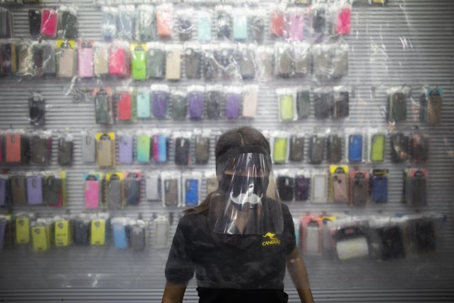 A woman wearing a protective face mask and face shield, stands behind of a plastic sheet set up as a measure to curb the spread of the new coronavirus, at a cell phone technology store in Caracas, Venezuela, Friday, June 5, 2020. President Nicolas Maduro and Venezuela's opposition, led by Juan Guaido, have agreed to measures for battling the new coronavirus to be overseen by international health workers, a first step in years toward cooperation between bitter political rivals for the benefit of the country. (Photo by Ariana Cubillos/AP Photo)