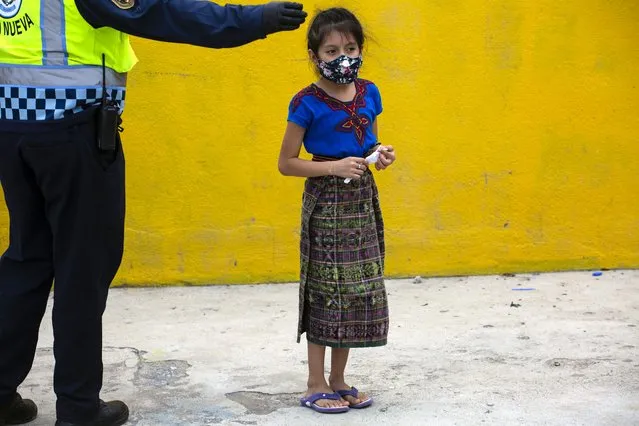 A child wearing a protective face mask, stands in line to receive a free meal in the Peronia neighborhood of Villa Nueva, Guatemala, Friday, July 24, 2020. The Villa Nueva City Hall delivers hot meals three times a week in a selected area of the neighborhood for residents who have been economically affected by the COVID-19 restrictions related to the government-ordered shutdowns. (Photo by Moises Castillo/AP Photo)