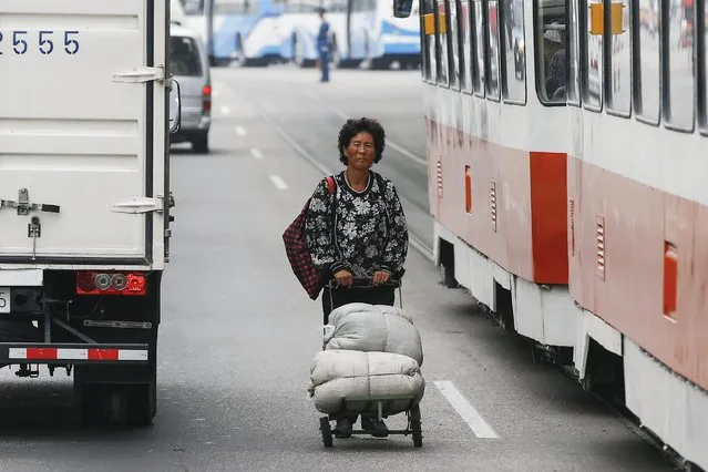 A woman pushes a cart between vehicles in downtown Pyongyang, North Korea October 8, 2015. Smartphones, traffic jams and modern, energy-saving lights casting a dim glow on the streets - North Korea's capital shows signs of change even as it prepares for a pageant of military muscle and propaganda of the kind the country is know for. (Photo by Damir Sagolj/Reuters)