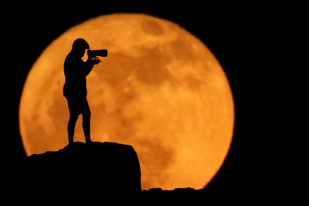 A photographer is silhouetted against the full moon known as the strawberry moon in Arinaga, on the island of Gran Canaria, Spain, on June 11, 2025. (Photo by Borja Suarez/Reuters)