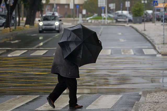 A man holds his umbrella against the wind-driven rain while crossing a street in Alges, just outside Lisbon, Tuesday, December 13, 2022. An Atlantic storm slammed into the Iberian peninsula, leaving behind a trail of destruction Tuesday, especially in the Portuguese capital Lisbon, before moving eastward into Spain. (Photo by Armando Franca/AP Photo)