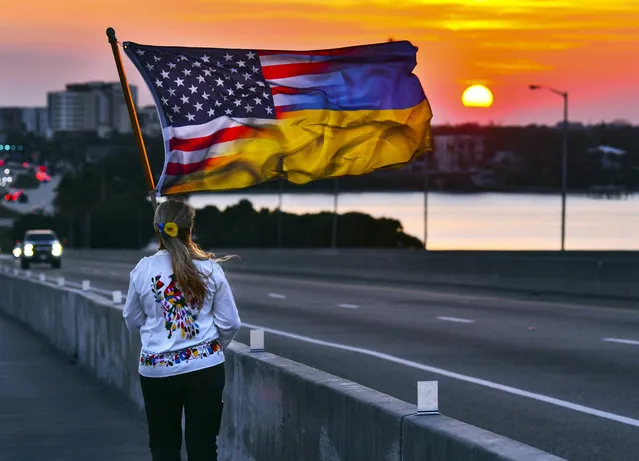 Olga Conover of Palm Bay, Fla., walks down the bridge at sunset carrying her merged American-Ukraine flag near the end of a march marking the one-year anniversary of Russia invading Ukraine,  late Thursday afternoon, February 23, 2022, in Melbourne, Fla. A small but passionate group of Ukraine supporters took the Melbourne Causeway to show their support, organized by the Ukrainian Space Coast group. (Photo by Malcolm Denemark/Florida Today via AP Photo)