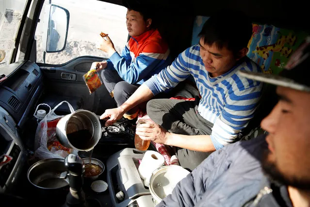 Three men eat a dinner of instant noodles and dried beef inside a truck at Khanbogd Soum, near the border with China, in the Gobi desert, Mongolia, October 31, 2017. Truckers cook, eat and sleep in vehicles covered in coal dust, many subsisting on the same meat soup that fuelled Genghis Khan's Mongol Horde more than eight centuries ago. (Photo by Bazarsukh Rentsendorj/Reuters)