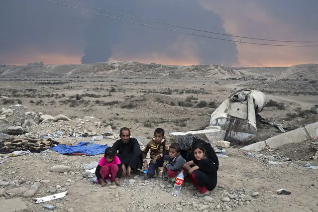 Internally displaced persons sit at a checkpoint as smoke rises from the burning oil wells in Qayyarah, about 31 miles (50 km) south of Mosul, Iraq, Sunday, October 23, 2016. (Photo by Marko Drobnjakovic/AP Photo)