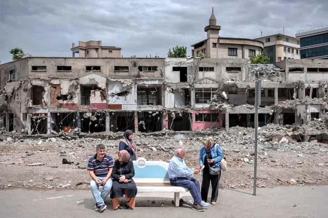 People wait at a bus stop in front of a destroyed building during the presidential runoff vote in the quake-hit city of Kahramanmaras, Turkey, on May 28, 2023. Turkey votes on May 28, 2023 in a historic runoff that Turkish President enters as the firm favourite to extend two decades of his Islamic-rooted rule to 2028. (Photo by Can Erok/AFP Photo)