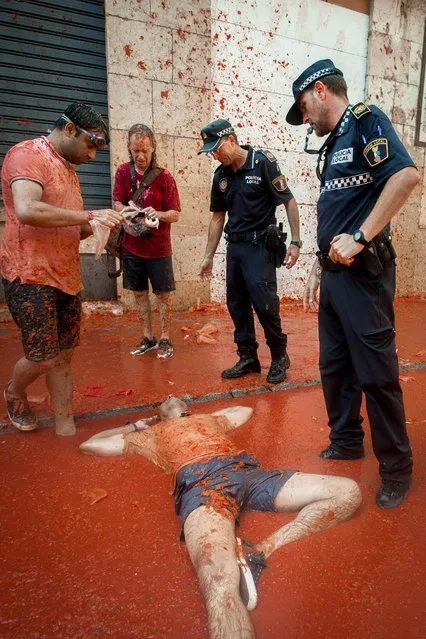 A reveller lies in tomato pulp as police stand above during the annual “Tomatina” festivities in the village of Bunol, near Valencia on August 31, 2016. Today at the annual Tomatina fiesta 160 tonnes of ripe tomatoes were offloaded from trucks into a crowd of 22,000 half-naked revellers who packed the streets of Bunol for an hour-long battle. (Photo by Biel Alino/AFP Photo)