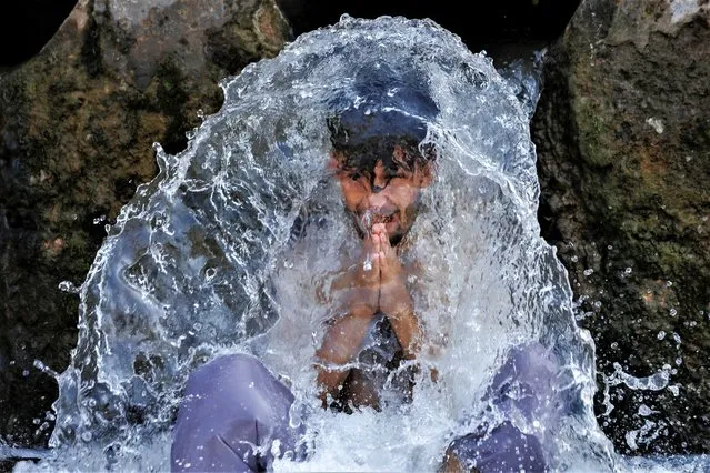 A man reacts as he cools off under a water pipe from a canal during hot and humid weather, in the outskirts of Peshawar, Pakistan on June 21, 2023. (Photo by Fayaz Aziz/Reuters)