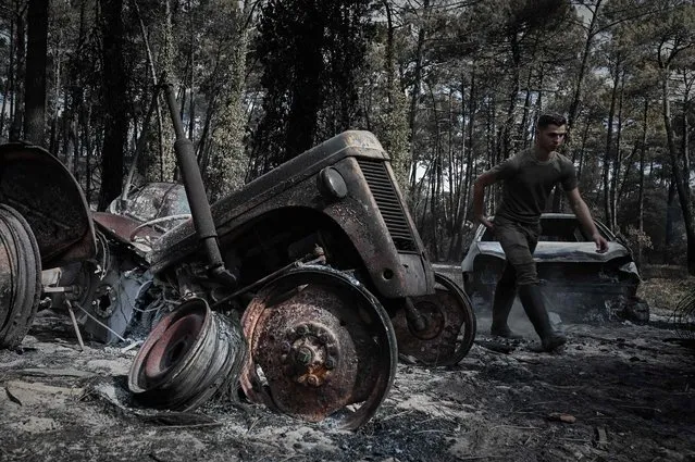 A French hunter walks past a burnt car during an operation to set up water points for wild animals on July 23, 2022 in a forest ravaged by a wildfire near Pyla sur Mer in Gironde, southwestern France. (Photo by Philippe Lopez/AFP Photo)