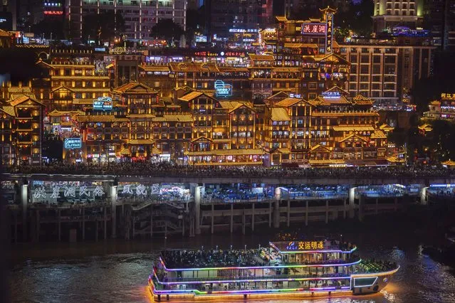 A ferry carries passengers by illuminated Hongyadong cluster of traditional looking buildings crowded with tourists during a weeklong national holiday in southwest China's Chongqing Municipality on September 30, 2023. (Photo by Chinatopix via AP Photo)