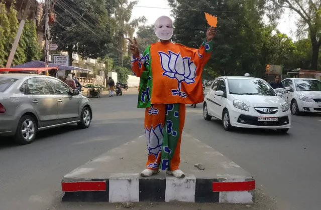 A supporter of India's Bharatiya Janata Party (BJP) wears a mask depicting the Indian Prime Minister Narendra Modi, and drapes himself with flags of BJP's symbol at a traffic signal in Bhopal, India, November 20, 2018. (Photo by Rajendra Jadhav/Reuters)