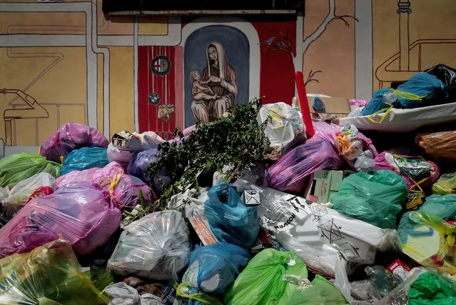 A painting of the Madonna and Infant Jesus is seen behind overflowing trash bins on the street as the city struggles with a garbage problem aggravated by the summer heat, on July 7, 2021 in Rome, Italy. (Photo by Stefano Montesi – Corbis/Corbis via Getty Images)
