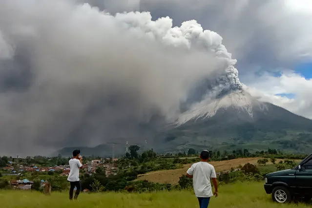 People look on as Mount Sinabung erupts spewing a massive column of smoke and ash as seen from Karo, North Sumatra, on July 28, 2021. The rumbling volcano on Indonesia‚Äôs Sumatra island on Wednesday shot billowing columns of ash and hot clouds down its slopes. (Photo by Muhammad Iksan Ginting/AFP Photo)