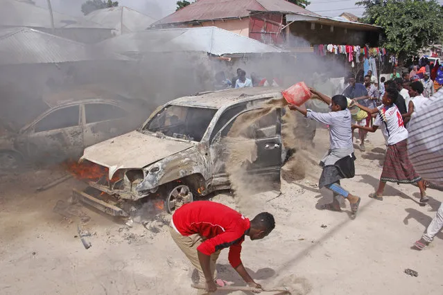 Somalis pour sand to smother a car fire after a car bomb in Mogadishu, Somalia, Sunday, December 16, 2018. At least one person was killed and others injured Sunday and nobody has claimed responsibility for the blast. (Photo by Farah Warsameh/AP Photo)