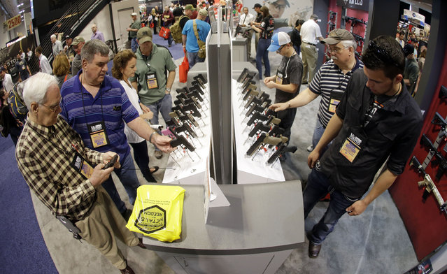 In this photo taken with a wide angle lens, people look at handguns displayed at the National Rifle Association convention Saturday, April 11, 2015, in Nashville, Tenn. (Photo by Mark Humphrey/AP Photo)