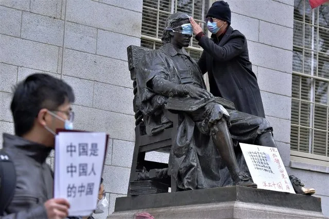 A man places a mask over the eyes of the John Harvard Statue in Harvard Yard as dozens of students and faculty demonstrate against strict anti-virus measures in China, Tuesday, November 29, 2022, at Harvard University in Cambridge, Mass. Protests in China, which were the largest and most wide spread in the nation in decades, included calls for Communist Party leader Xi Jinping to step down. (Photo by Josh Reynolds/AP Photo)