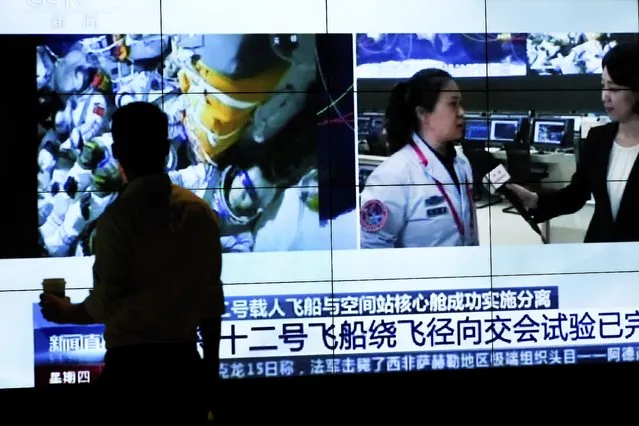 A man is silhouetted as he watches a TV screen showing CCTV broadcasting a news of Chinese astronauts sit inside the Shenzhou-12 manned spacecraft preparing to return to earth, at a shopping mall in Beijing, Thursday, September 16, 2021. (Photo by Andy Wong/AP Photo)