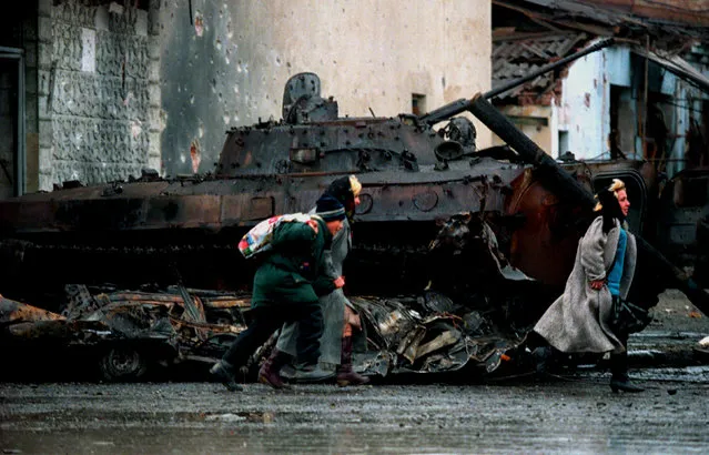 Chechen civilians run in front of a destroyed Russian army APC as they flee from central Grozny, during fighting January 4, 1995. (Photo by Yannis Behrakis/Reuters)
