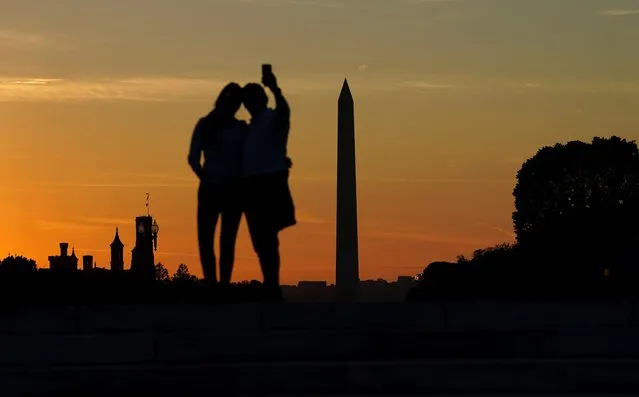 The sky goes orange behind the Washington Monument and the Smithsonian Castle as a couple pose for a sunset selfie in Washington U.S., October 14, 2021. (Photo by Kevin Lamarque/Reuters)
