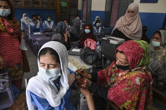 A health worker inoculates a student with a dose of Pfizer vaccine against the Covid-19 coronavirus at a school in Lahore on October 5, 2021, after the government began a drive to vaccinate children aged 12 and above. (Photo by Arif Ali/AFP Photo)