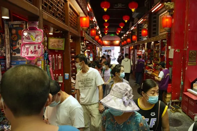 Visitors wearing face masks look at souvenir shops in a neighborhood popular with tourists in central Beijing, Tuesday, August 3, 2021. From the Great Wall to the picturesque Kashmir valley, Asia's tourist destinations are looking to domestic visitors to get them through the COVID-19 pandemic's second year. With international travel heavily restricted, foreign tourists can't enter many countries and locals can't get out. (Photo by Mark Schiefelbein/AP Photo)
