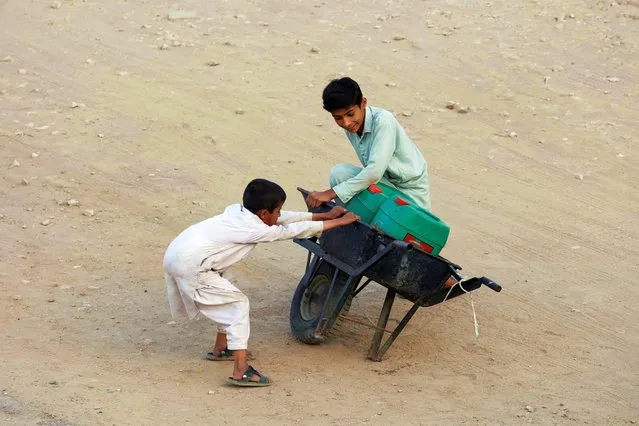 Children balance a wheelbarrow with water jerrycans, which they filled from a nearby hand pump, as they head home in Karachi, Pakistan on February 26, 2024. (Photo by Akhtar Soomro/Reuters)