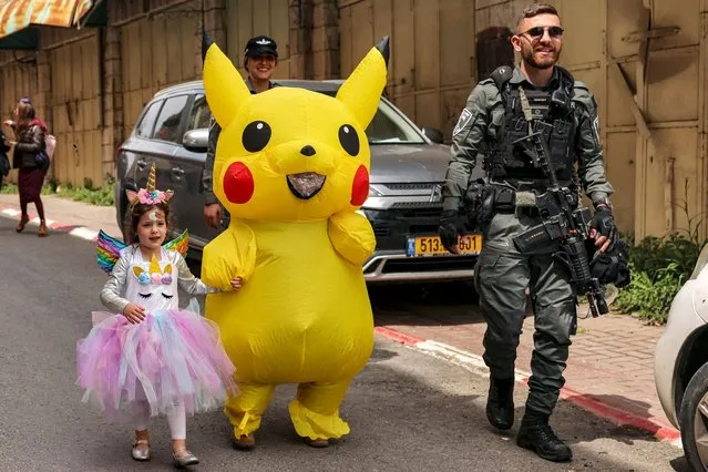 An Israeli border guard escorts a girl dressed as a unicorn and another reveller in Pikachu costume along Al-Shuhada street, which is largely closed to Palestinians, in the divided city of Hebron in the occupied West Bank during celebrations by Israeli settlers of the Jewish holiday of Purim on March 24, 2024. (Photo by Hazem Bader/AFP Photo)