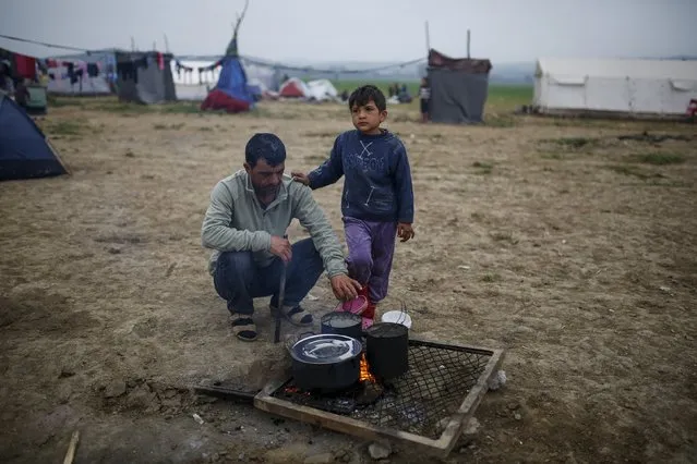 A child stands by his father, who is preparing a meal, at a makeshift camp for migrants and refugees at the Greek-Macedonian border near the village of Idomeni, Greece, April 3, 2016. (Photo by Marko Djurica/Reuters)