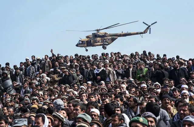 An Afghan National Army helicopter flies over  men attending in the burial of Afghanistan's influential Vice President Mohammad Qasim Fahim during his funeral procession in Kabul, Afghanistan, on March 11, 2014. (Photo by Massoud Hossaini/Associated Press)