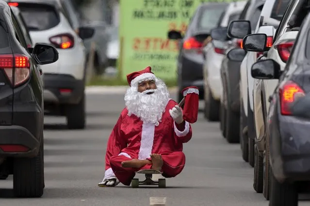 Jose Ivanildo, who lost the use of his legs due to infantile paralysis, begs for money at a traffic light dressed as Santa Claus in Brasilia, Brazil, Tuesday, December 21, 2021. The 48-year-old, known as “Ivanildo do Skate”, said that the COVID-19 pandemic has made people scared to open their windows. (Photo by Eraldo Peres/AP Photo)