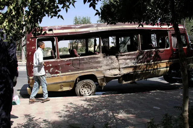 A boy walks past the wreckage of a bus following a suicide bombing in Kabul on July 25, 2019. At least 10 people – including several women and a child – were killed and 41 others wounded by a series of blasts that rocked the Afghan capital on July 25 ahead of the election season. (Photo by AFP Photo/Stringer)