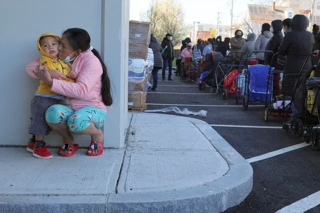 Elvia Garcia kisses her two-year-old son Joshua while they wait with hundreds of other residents to pick up free groceries from the food pantry run by La Colaborativa in Chelsea, Massachusetts, U.S., April 20, 2022. (Photo by Brian Snyder/Reuters)